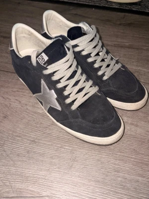 Golden goose ballstar - Ballstar custom made i butik, Snygga mörkblå sneakers i mocka med en stor silverfärgad stjärna på sidan och matchande silverfärgade detaljer vid hälen. Skorna har vita sulor och gråvita skosnören. Perfekta för dig som gillar en stilren men ändå unik look.