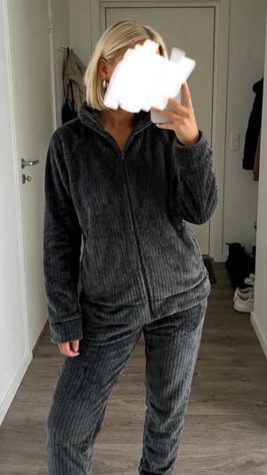 Mysig grå loungewear-set - Säljer ett supermjukt och fluffigt loungewear-set i mörkgrå färg. Setet består av en ziptröja med hög krage och matchande byxor, båda i ribbad plysch. Perfekt för hemmamys eller chill dagar. Materialet är lent och värmande.