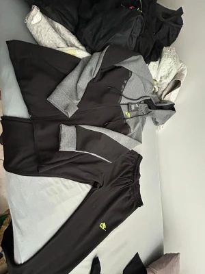 Nike svart och grå  - Snyggt träningsset från Nike med svart och grå zip-hoodie och matchande byxor. Hoodien har dragsko i huvan och Nike-logga i neon på bröstet. Byxorna har elastisk midja och liten Nike-logga. Perfekt för gymmet eller chill. Jätte bra nytt med prislapp inte använd