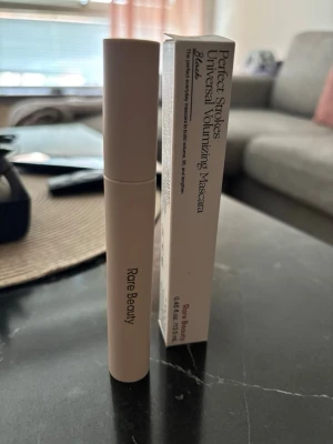 Rare Beauty Perfect Strokes Mascara - Säljer en Rare Beauty Perfect Strokes Universal Volumizing Mascara i färgen svart. Tuben är stilren och beige med guldtext. Förpackningen är av kartong och matchar tubens design. Innehåller 13,5 ml. Perfekt för dig som vill ha volym och definierade fransar.