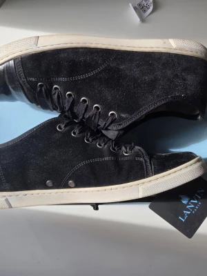 Svarta sneakers från Lanvin - Snygga svarta sneakers från Lanvin i mocka med vita gummisulor och svarta skosnören. Klassisk låg modell med diskreta sömmar och metallöljetter. Perfekta för dig som gillar stilrena och exklusiva skor.