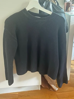 Svart stickad tröja  - En enkel och stilren svart stickad tröja med rund halsringning och ribbade muddar vid ärmslut och nederkant. Tröjan har en rak passform och är perfekt för lager på lager under kyliga dagar. Materialet ser mjukt och mysigt ut.
