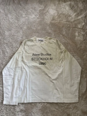 Acne Studios - Sleeve - Vit sleeve från Acne Studios med tryck 'STOCKHOLM 1996' på bröstet. Klassisk rund hals och avslappnad passform. Perfekt för dig som gillar minimalistisk och stilren design.