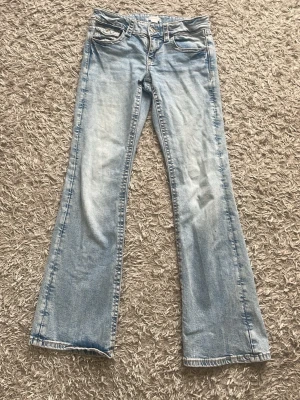 Ljusblå bootcut jeans - Säljer ett par ljusblå bootcut jeans med klassisk femficksdesign och snygga detaljer på bakfickorna. Jeansen har en lätt tvättad look och är tillverkade i denim med skön passform. Storlek 158