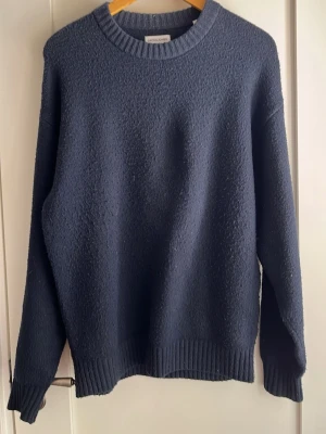 Mörkblå stickad tröja från Jack & Jones - En enkel och stilren mörkblå stickad tröja med rund halsringning och ribbade muddar vid ärmslut och nederkant. Tröjan har en rak passform och är perfekt för lager-på-lager under kyliga dagar. Storlek S men sitter som M