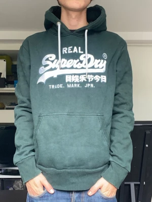 Superdry hoodie - En riktigt snygg mörkgrön hoodie från superdry i storlek L, sitter som M. Han på bilden är 179. Mycket gott skick. Har du några frågor? Fråga på