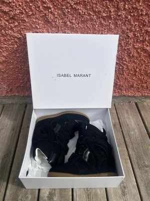 Isabel Marant svarta sneakers med kardborre - Svarta sneakers från Isabel Marant med högt skaft och cool design. Skorna har flera kardborreband och en kontrasterande ljusbrun sula. Materialmix av mocka och läder ger en lyxig känsla och streetstyle-vibe.