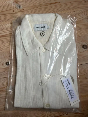 Vit skjorta från East West - Klassisk vit skjorta från East West i storlek S. Skjortan har krage, knäppning framtill och är tillverkad i ett lätt, krinklat bomullstyg. Nypris 699kr