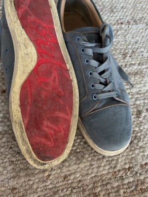 Blå mockasneakers med röd sula - Snygga blå sneakers i mocka med klassisk låg profil och vita kanter. Skorna har en unik röd sula med mönster och matchande blå skosnören. Perfekta för dig som vill ha en stilren men ändå unik look.