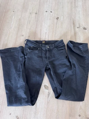 Svarta bootcut jeans från Lee - Säljer ett par svarta bootcut jeans från Lee med klassisk femficksmodell och normal midja. Jeansen har en lätt utsvängd passform nedtill och är tillverkade i ett mjukt denimtyg som sitter snyggt på benen.