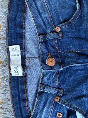 Blå jeans från Gina Tricot - Snygga blå jeans från Gina Tricot, modell Perfect Jeans. Klassisk femficksdesign med kopparfärgade knappar och kontrastsömmar. Jeansen har normal midja och är gjorda i ett mjukt denimtyg som sitter skönt. Perfekta till alla dina outfits!