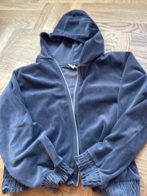 Mjuk mörkgrå hoodie från Lindex - Säljer en mjuk och skön mörkgrå hoodie från Lindex med dragkedja framtill. Hoodien har luva och breda muddar vid ärmslut och nederkant. Perfekt för chill dagar eller när du vill ha något bekvämt och stilrent.