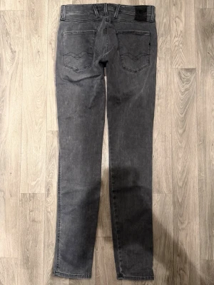 Replay Anbass Hyperflex Grå Jeans W30/L34 - Slim Fit - Replay Anbass Hyperflex grå jeans med slim fit-passform som sitter smalt och bekvämt och funkar till allt, storlek W30/L34, midja 38,5 cm, ytterbenslängd 109,5 cm, benöppning 15 cm, modellen är 185cm & väger 65kg, i fint skick.
