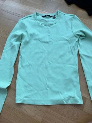Mintgrön ribbad långärmad topp - Snygg mintgrön långärmad topp från Vero Moda i ribbad bomullsmix. Perfekt att styla med jeans eller kjol för en fräsch look. Enkel rund halsringning och figurnära passform.