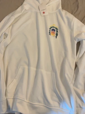 Vit hoodie från Casablanca - Vit hoodie från Casablanca med färgglatt tryck på bröstet som föreställer en portal och blad. Klassisk känguruficka framtill och huva. Perfekt för dig som gillar stilrena plagg med en twist.