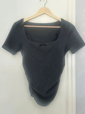 Mörkgrå croppad t-shirt med rosett - Grå T-shirt med spets i storlek M. Använd bara en gång🥰