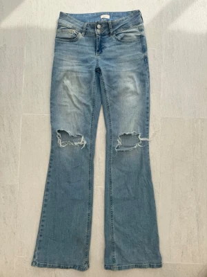 Ljusblå bootcut jeans från Nelly - Säljer ett par ljusblå bootcut jeans från Nelly med slitna detaljer och stora hål vid knäna. 