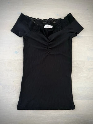 Svart topp med spets - Snygg svart ribbad topp med offshoulder-design och spetskant upptill. (Rätt liten i storlek)💗
