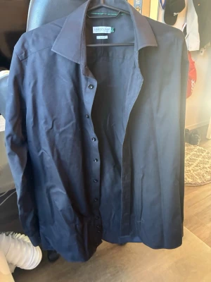 Mörkblå skjorta från J. Harvest & Frost - Snygg mörkblå skjorta från J. Harvest & Frost i slim fit-modell. Skjortan har klassisk krage, långa ärmar och knappar framtill. Perfekt för dig som gillar stilrena och enkla plagg. Tillverkad i mjuk bomull för skön känsla hela dagen.