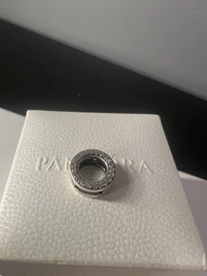 Pandora reflextions clip berlock - Snygg rund berlock från Pandora i silverfärg med gnistrande små stenar runt hela kanten. Perfekt att sätta på ett armband för att ge det extra bling. Klassisk och stilren design som passar till många olika stilar. 