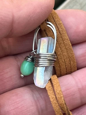 Halsband med kristall och grön pärla - Unikt halsband med en regnbågsskimrande kristall och en liten grön pärla, båda infattade i silverfärgad metalltråd. Hänget sitter på ett brunt mockaband som ger en bohemisk känsla. Perfekt för dig som gillar naturmaterial och statement-smycken.