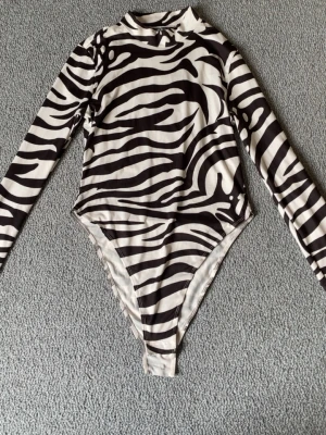 Skit cool zebra body - Snygg body med zebramönster i svart och vitt. Modellen har lång ärm, hög hals och åtsittande passform. Tillverkad i ett stretchigt material som sitter bekvämt mot kroppen. As cool till er par jeans, och massa annat. Hör av er vid intresse!💕 postar inom 24 h