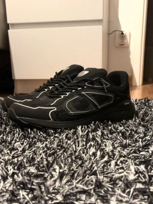 Svarta sneakers med vita detaljer - Snygga svarta sneakers med vita kontrastdetaljer och stora CD-loggor på sidorna. Dom är lite slitna på utsidan men de syns inte om man inte tittar nära dom eftersom dom e svarta, tyget på sulan vid hälen har lossnat lite men de syns inte heller eftersom man har på sig dom och jag har ingen box eller påse. Därför säljer jag dom billigt. Pris kan diskuteras