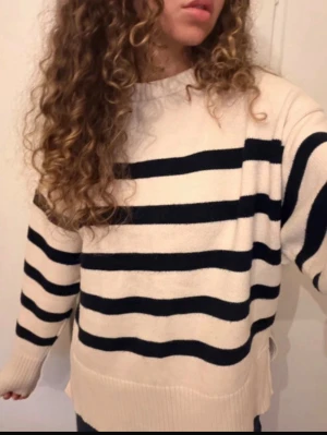Vit stickad tröja med svarta ränder - Säljer en oversized beige stickad tröja med breda svarta horisontella ränder. Tröjan har rund halsringning, långa ärmar och ribbade muddar. 