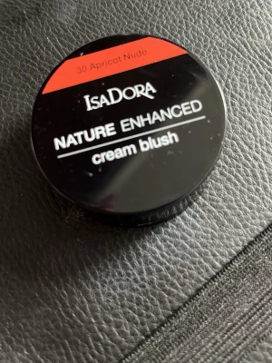 Isadora Nature Enhanced Cream Blush - Krämrouge från Isadora i färgen 30 Apricot Nude. Kommer i en rund svart dosa med spegel i locket. Färgen är en varm aprikos-nude ton som ger ett naturligt glow till kinderna. Konsistensen är krämig och lätt att blenda ut för en fräsch look. Använts fåtal gånger.