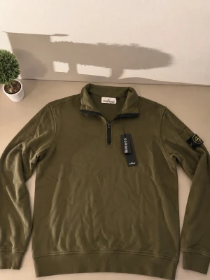 Olivgrön half-zip tröja Stone Island - Snygg olivgrön tröja från Stone Island med half-zip och hög krage. Tröjan har lång ärm, ribbade muddar och den klassiska Stone Island-loggan på vänster ärm. Perfekt för en avslappnad men stilren look.