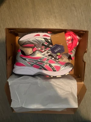 Asics gel kayano 14 - Snygga Asics sneakers i silver och rosa med vita och svarta detaljer. Skorna har meshpaneler för bra ventilation och en chunky sula för skön komfort. Medföljer extra rosa skosnören. Perfekta för dig som vill sticka ut med färg och sportig stil.