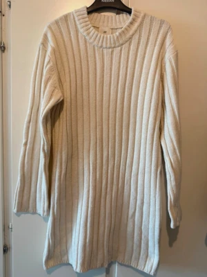 Beige ribbstickad lång klänning - Säljer en beige ribbstickad lång klänning med rund halsringning och långa ärmar. Klänningen har en relaxed fit. Materialet känns mjukt och skönt mot huden, och den neutrala färgen gör den enkel att matcha.