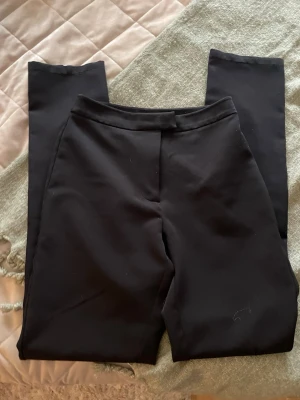Svarta kostymbyxor från NA-KD - Snygga svarta kostymbyxor från NA-KD med rak passform och klassisk midja. Byxorna har en stilren look utan synliga fickor framtill och stängs med hake och dragkedja. Perfekta för en clean och trendig outfit.