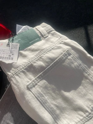 Vita raka jeans med hög midja - Säljer ett par vita jeans med rak passform och hög midja. Jeansen har klassiska fem fickor och bälteshällor. Materialet är kraftig denim som ger en snygg och stilren look. Perfekta för dig som vill ha ett par ljusa jeans till garderoben.