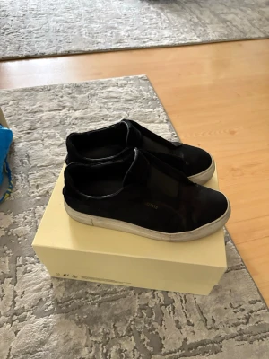 Svarta slip-on sneakers med vit sula - Snygga svarta slip-on sneakers med tjock vit sula. Skorna har en minimalistisk design utan snörning och är tillverkade i mockaliknande material. Perfekta för en clean och stilren look till vardagsoutfiten. Kommer med boxen, dustbag och andra tillbehör. Kan sänkas vid snabb affär. Kan tvättas om man säger till. De säljs inte längre så är lite sällsynta. 