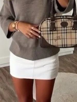 Burberry handväska  - Snygg handväska i klassiskt beige rutigt mönster med bruna läderdetaljer och dubbla handtag. Väskan är ca 30 cm bred och har en oval form. Perfekt accessoar för att lyfta din outfit med en tidlös look.