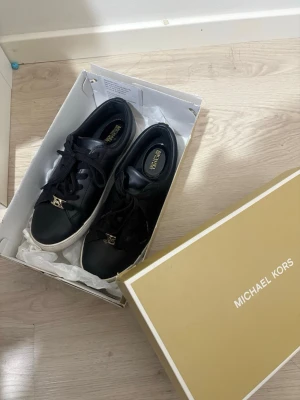 Svarta Michael Kors sneakers i skinn - Stilrena svarta sneakers från Michael Kors i mjukt skinn med vita sulor och svarta skosnören. 