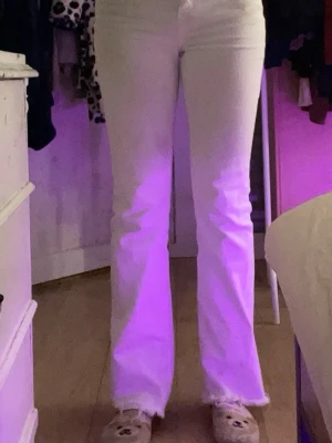 Vita bootcut jeans med rå kant - Säljer ett par vita bootcut jeans med hög midja och råa, fransiga benslut. Jeansen har klassisk femficksdesign och stängs med knapp och dragkedja. Perfekta för dig som vill ha en clean och trendig look.