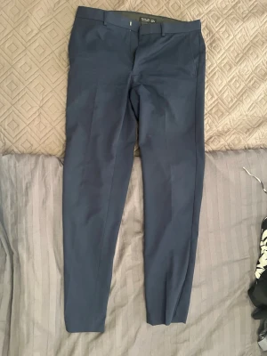 Mörkblå kostymbyxor/chinos Primark - W34/L34 Slim Fit - Klassiska mörkblå byxor från Primark i slim fit-modell. Mycket bra passform och passar fint till både vardags och finare tillfällen. De har snygga pressveck framtill.  Skick: Sparsamt använda, i mycket fint skick utan skador eller fläckar.  Färg: Marinblå (Mörkblå)  Modell: Slim Fit  Storlek: W34 / L34 (Midja 34 tum, Benlängd 34 tum). Det här är en "lång" storlek.  Märke: Primark ✨ Kika gärna på mina andra varor på sidan! Jag säljer just nu av en stor del av garderoben med allt från märkeskläder