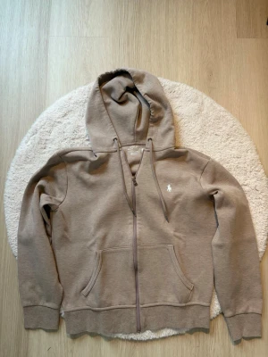 Beige ralph lauren zip hoodie - Säljer nu min beiga Ralph lauren zip hoodie pågrund av att den blivit för liten. Den är i stl S men passar mer som en XS. Den är i topp skick därför priset men det är inte helt hugget i sten!