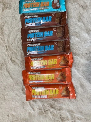 Probrands proteinbars mix - Säljer ett gäng Probrands proteinbars i olika smaker: chocolate, coconut choco och toffee caramel. Perfekt som mellanmål eller efter träning. Färgglada förpackningar i brunt, blått och orange. Säljes som ett paket.