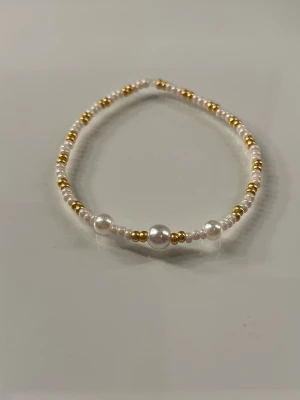 Pärlarmband med vita och guldfärgade pärlor - Snyggt armband med små vita och guldfärgade pärlor i olika storlekar. Armbandet har en elastisk tråd och en enkel, stilren design som passar till många olika looks. Perfekt accessoar för dig som gillar en klassisk men trendig stil.