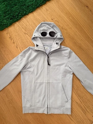 C.P. Company Hoodie - Unik ljusgrå CP Company hoodie. Knappt använd. Passar personer som är runt 175-183 väldigt bra. Är du lite längre/kortare borde det gå bra ändå. 