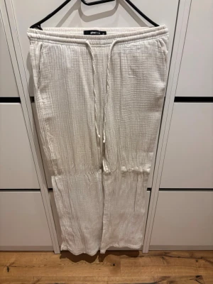 Vita linnebyxor från Gina Tricot - Säljer ett par vita linnebyxor från Gina Tricot i storlek XS. Byxorna har resår i midjan med dragsko och är tillverkade i ett luftigt, strukturerat tyg. Perfekta för en avslappnad och trendig look. Dom har blivit vikta eftersom de har hängt på en galge annars är byxorna i samma stil som resten. 