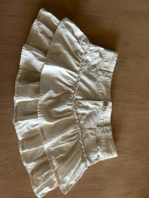 Vit jeans kjol  - Snygg vit kortkjol med volanger och bred linning. Kjolen är från bershka. Den är i jeans material. Super snygg med vilken outfit som helst. Längden i midjan är 38 cm. Skulle passa bra för nån som har storlek Small. Priset kan diskuteras.