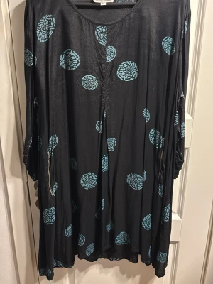Svart långklänning med blått mönster - Svart långklänning med löst fall och blått blommigt mönster. Klänningen har rund halsringning och långa ärmar. Materialet känns mjukt och följsamt, perfekt för dig som gillar en avslappnad stil.