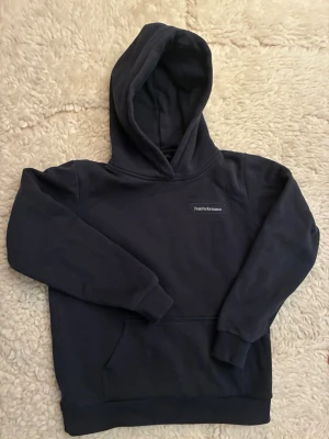 Mörkblå hoodie från Peak Performance - Mörkblå hoodie från Peak Performance med klassisk huva och magficka. Tröjan har ribbade muddar vid ärmslut och nederkant samt en liten logotyp på bröstet. Perfekt för en avslappnad och sportig stil. Orginal pris 599kr.