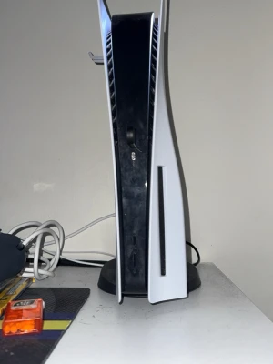 PlayStation 5 konsol med skivläsare - Säljer en PlayStation 5 konsol med skivläsare. Konsolen har en futuristisk design med vita sidopaneler och svart mittdel i plast. Perfekt för gaming med stöd för de senaste spelen och snabb SSD. Står på medföljande ställ. Rosa handkontroll medföljer samt det går att sänka priset!