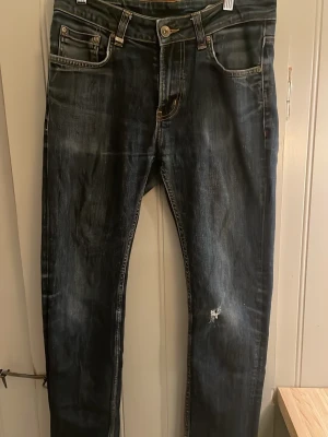 Mörkblå slitna jeans herr - Säljer ett par mörkblå jeans med slitningar och tvättade detaljer. Jeansen har fem fickor, knappgylf och smal passform. Materialet är klassisk denim i bomull. Perfekta för en avslappnad och trendig look.