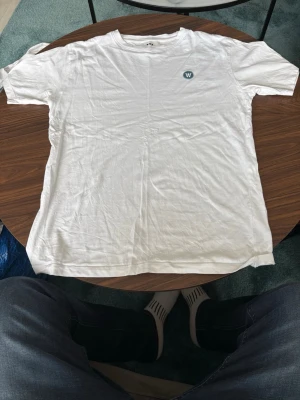 Vit t-shirt från Wood Wood - Vit t-shirt från Wood Wood med liten W-logga på bröstet. Klassisk passform och rund halsringning. Tillverkad i mjuk bomull, perfekt för en clean och enkel stil.